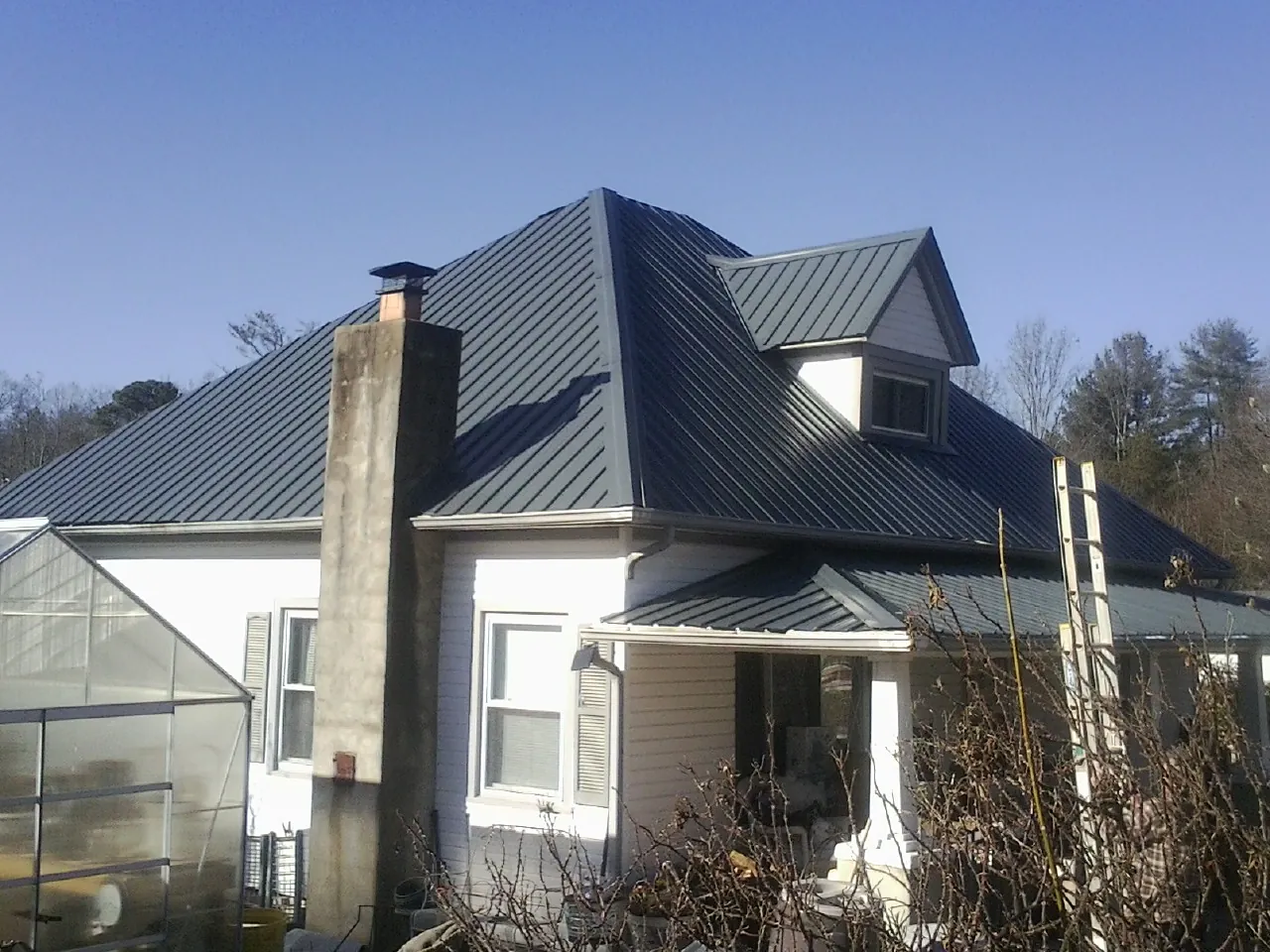 Dark blue standing seam metal roof on a white farmhouse with dormer — Slate & Tile Roof Repair by Roofing Brothers in Manton