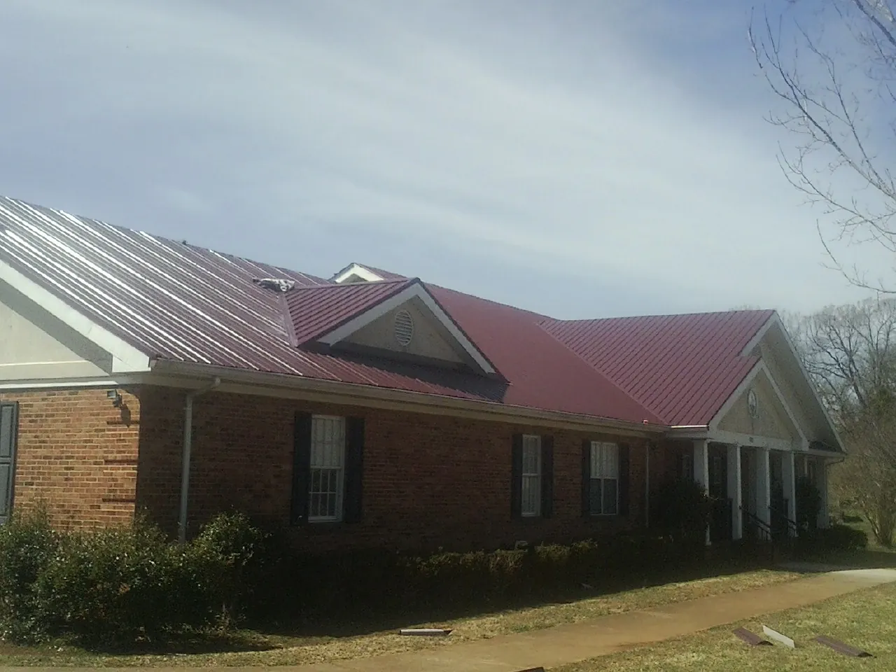 Red metal roof with gabled entries on a long brick building, from a Hail Damage Roof Repair job in Manton