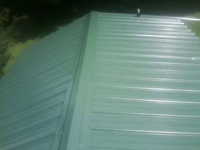 New green metal panels meeting at the ridge of a roof — Flat Roof Repair work by our crew in Manton